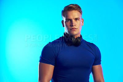 Buy stock photo Studio portrait of a handsome young male athlete posing with headphones around his neck against a blue background