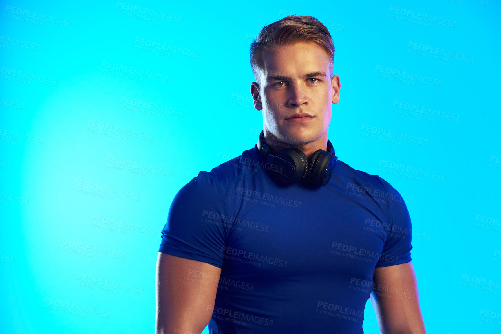 Buy stock photo Studio portrait of a handsome young male athlete posing with headphones around his neck against a blue background