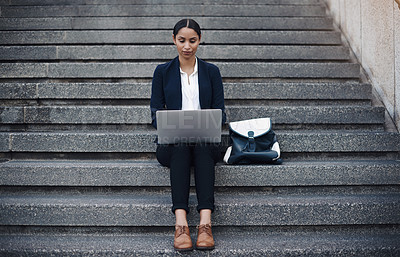 Buy stock photo Shot of a young businesswoman using a laptop on the stairs against a city background