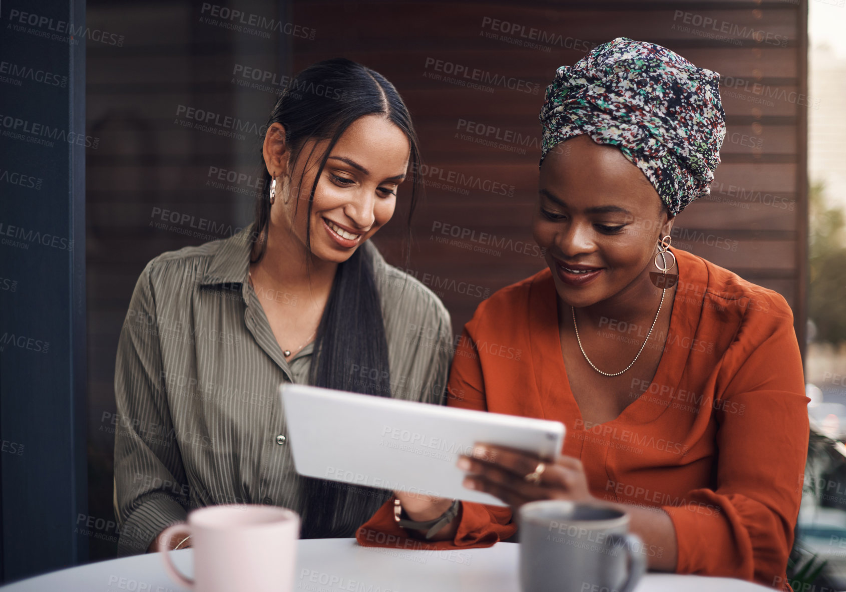 Buy stock photo Cropped shot of two attractive businesswomen working on a tablet together in their office