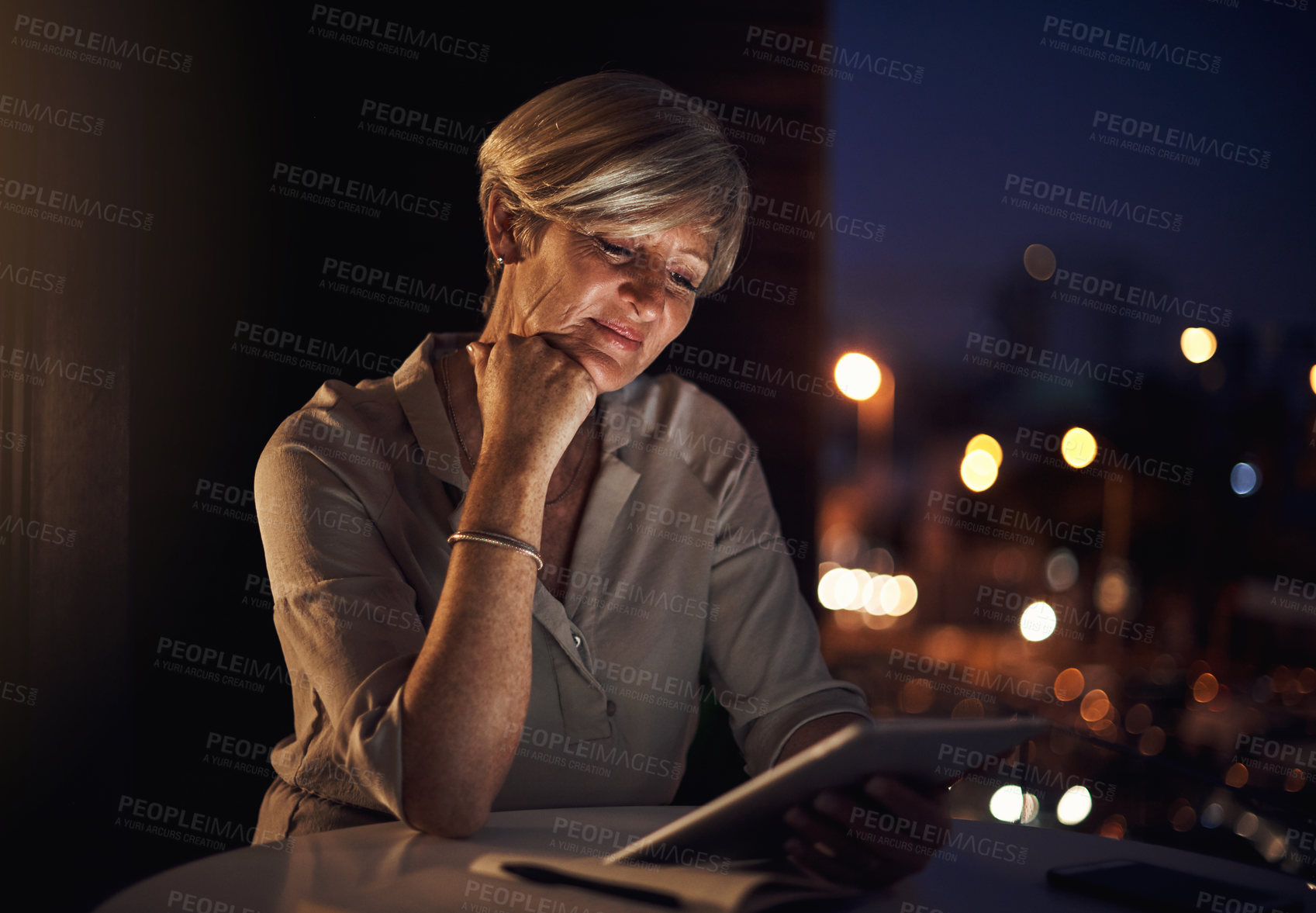 Buy stock photo Cropped shot of an attractive mature businesswoman using her tablet while working late in the office