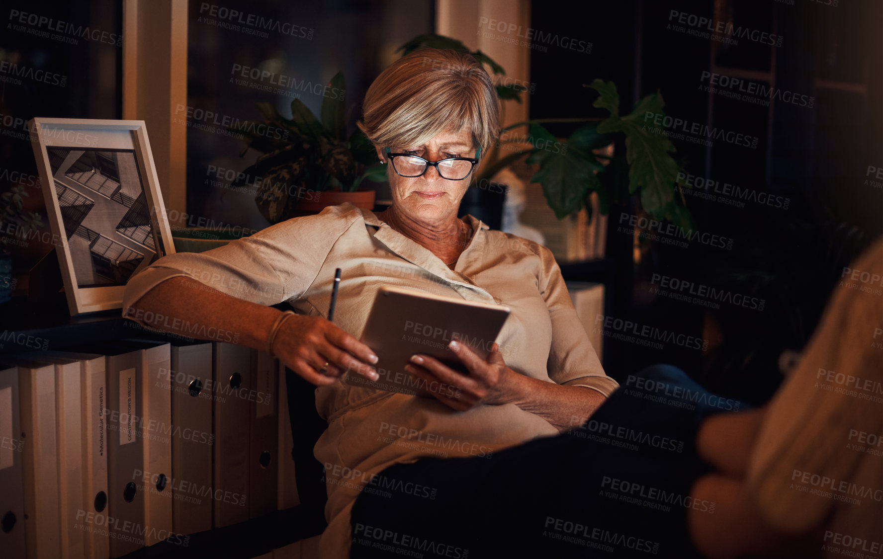 Buy stock photo Cropped shot of an attractive mature businesswoman looking relaxed while using her tablet late at night in the office
