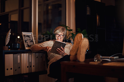 Buy stock photo Full length shot of an attractive mature businesswoman looking relaxed while using her tablet late at night in the office