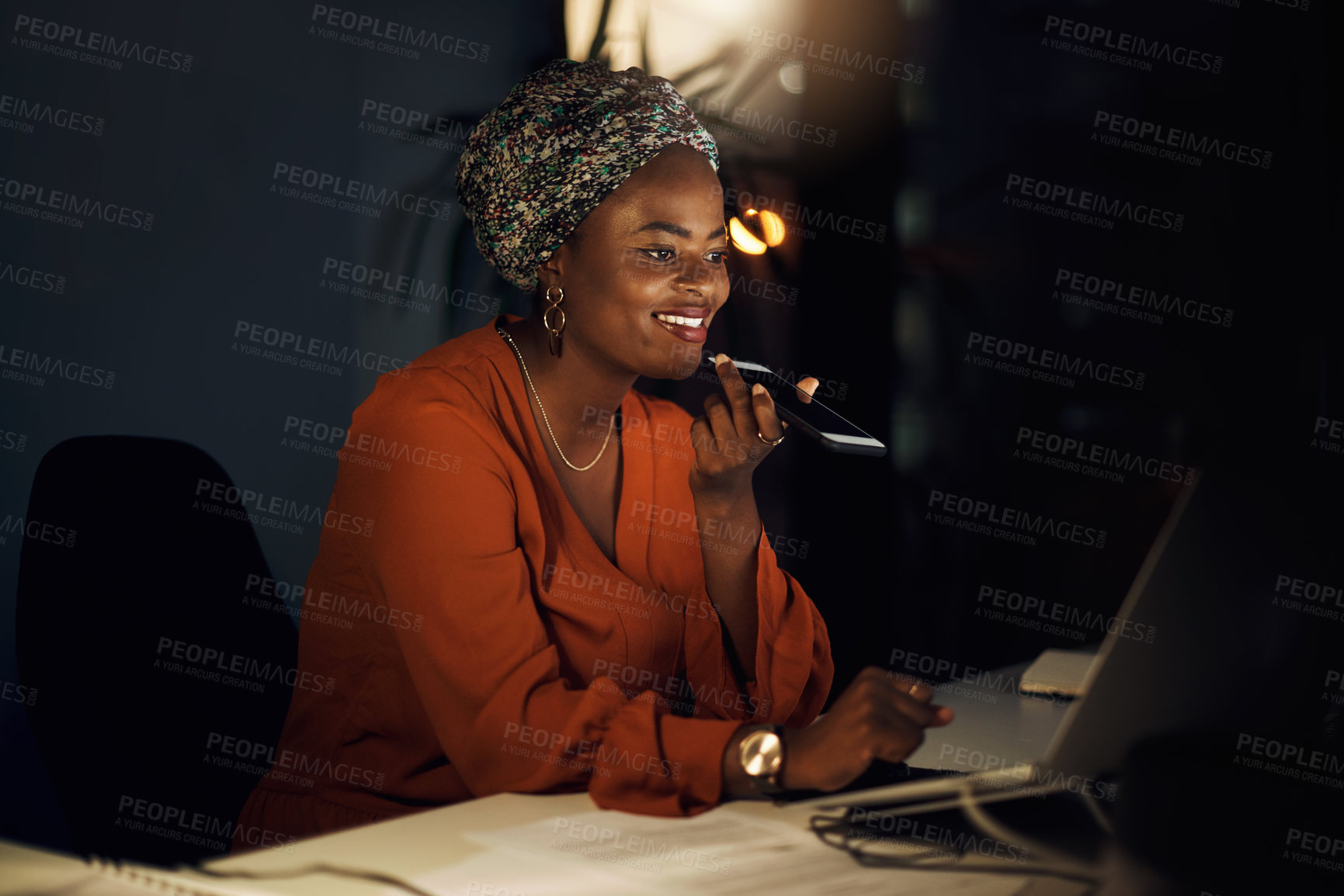 Buy stock photo Shot of a young businesswoman talking on a cellphone while using a laptop in an office at night