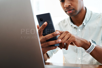 Buy stock photo Shot of a young businessman using a smartphone and laptop at his desk in a modern office