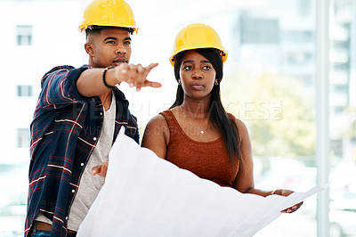 Buy stock photo Shot of a young man and woman going over a blueprint in a modern office