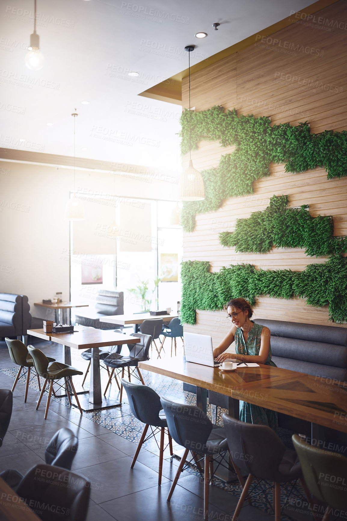 Buy stock photo Shot of a young woman using a laptop while working at a cafe