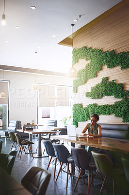 Buy stock photo Shot of a young woman using a laptop and writing in a notebook while working at a cafe