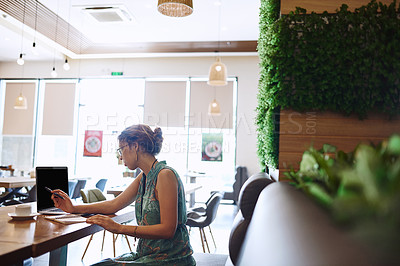 Buy stock photo Shot of a young woman using a laptop while working at a cafe