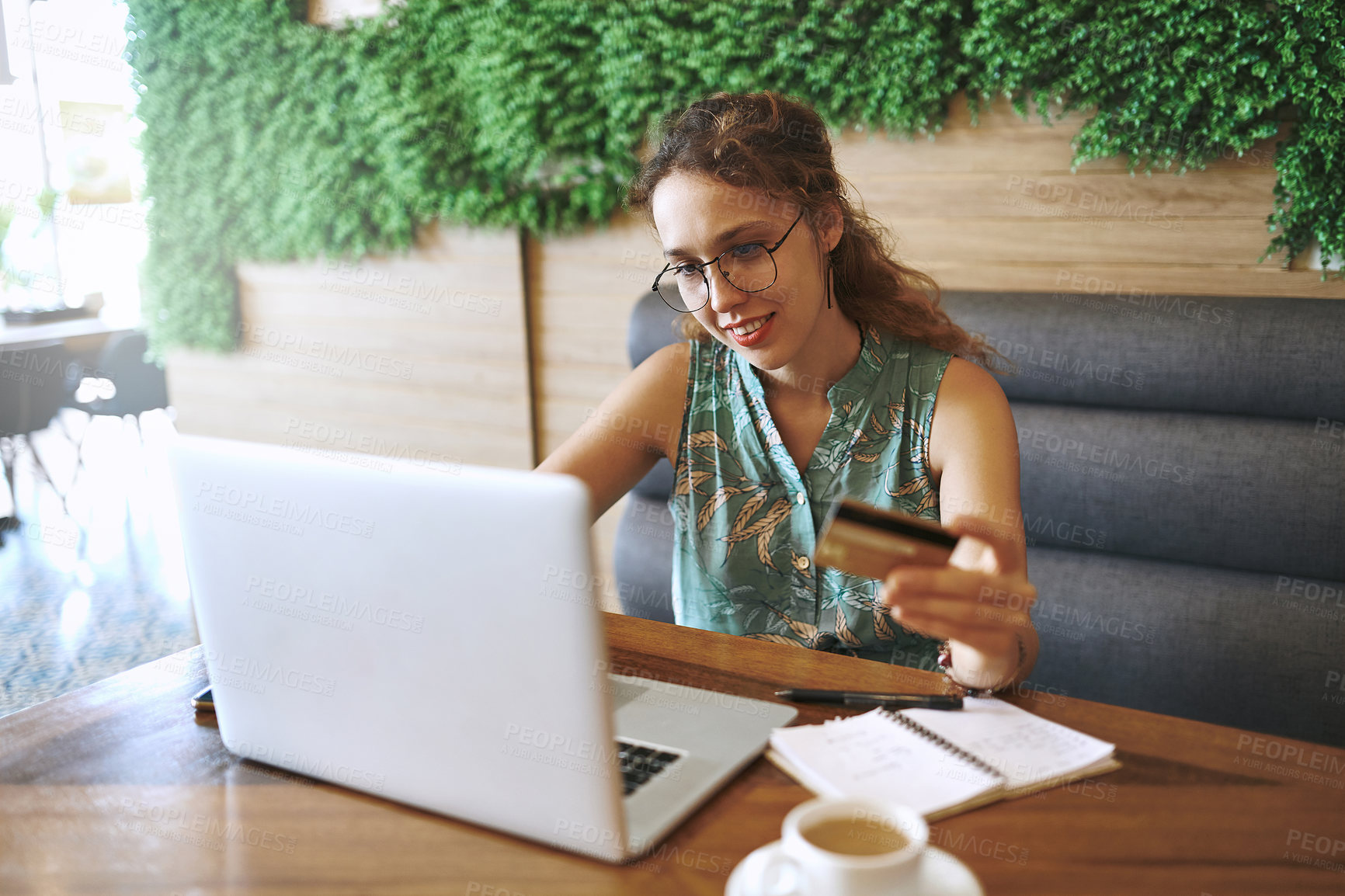 Buy stock photo Shot of a young woman using a laptop and credit card while working at a cafe