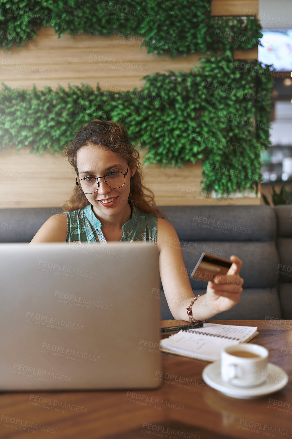 Buy stock photo Shot of a young woman using a laptop and credit card while working at a cafe