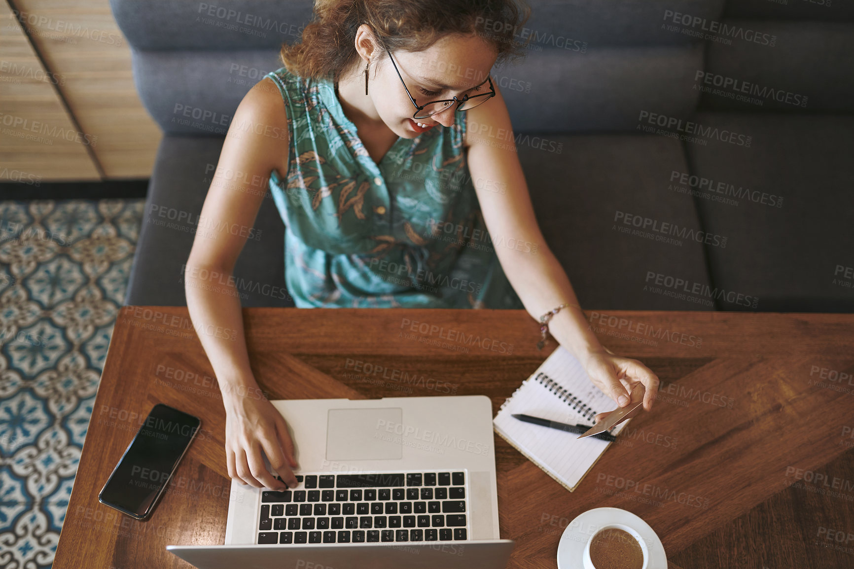 Buy stock photo High angle shot of a young woman using a laptop and credit card while working at a cafe