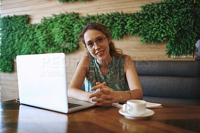 Buy stock photo Shot of a young woman using a laptop while working at a cafe