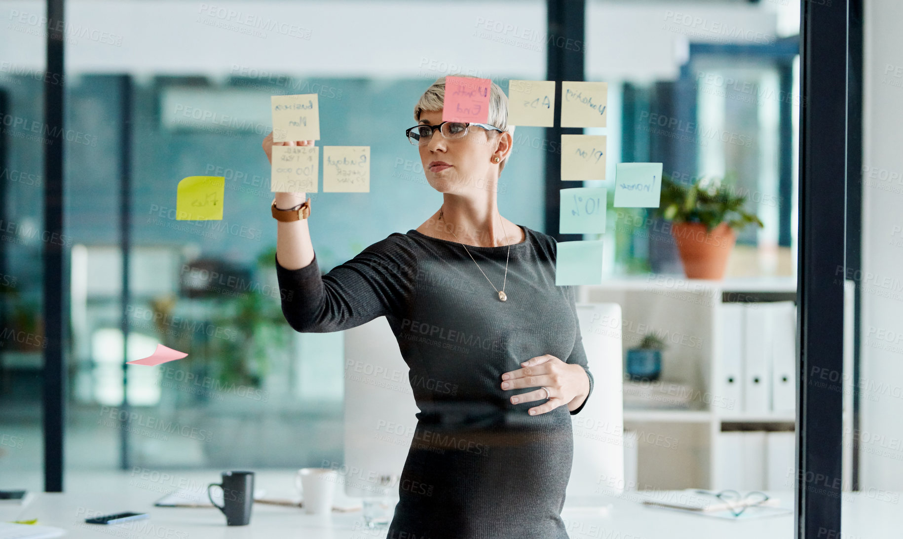 Buy stock photo Shot of a pregnant businesswoman brainstorming with notes on a glass wall in an office