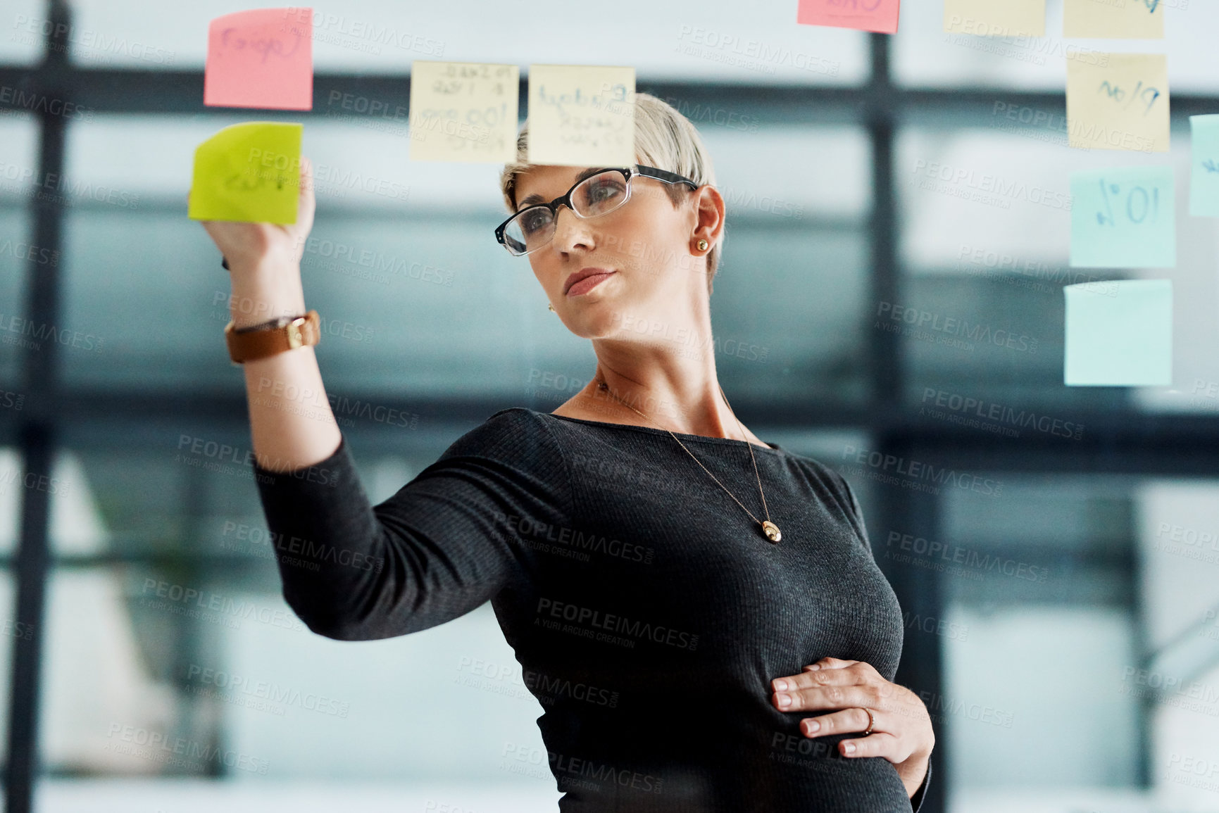 Buy stock photo Shot of a pregnant businesswoman brainstorming with notes on a glass wall in an office