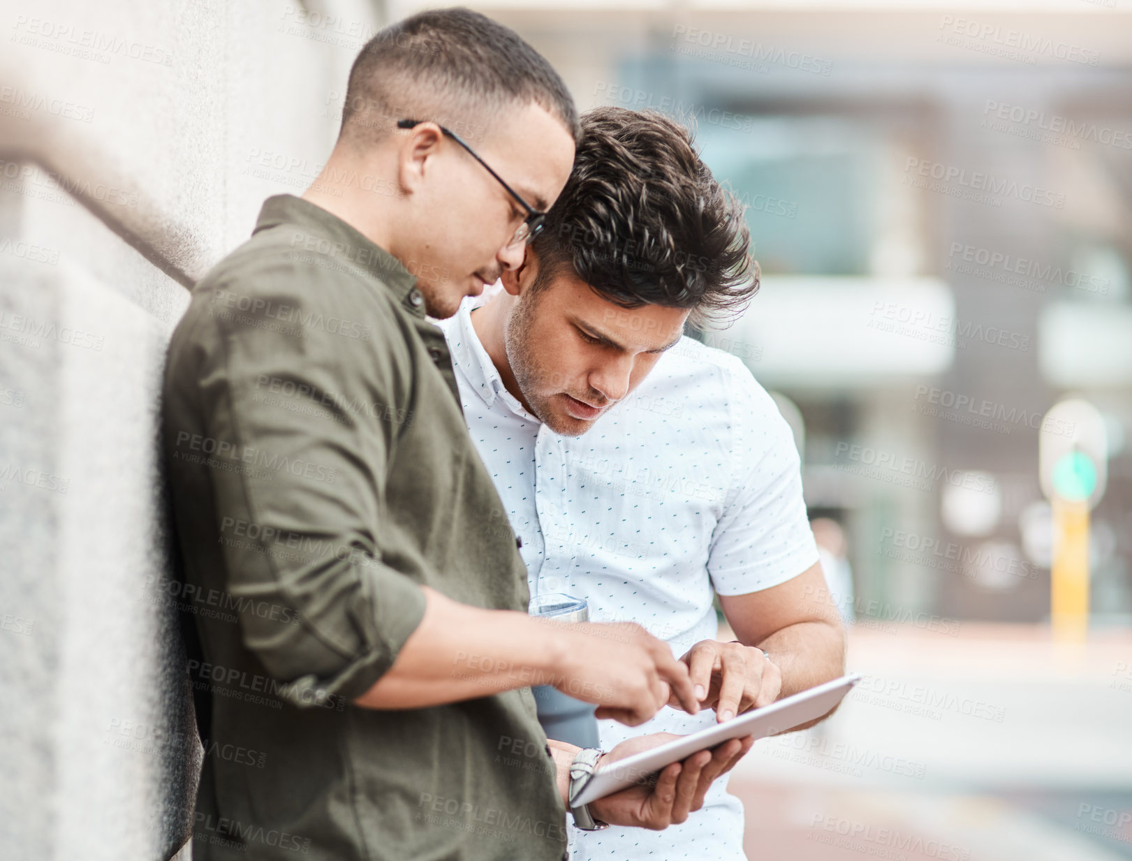 Buy stock photo Shot of two young businessmen using a digital tablet together against an urban background