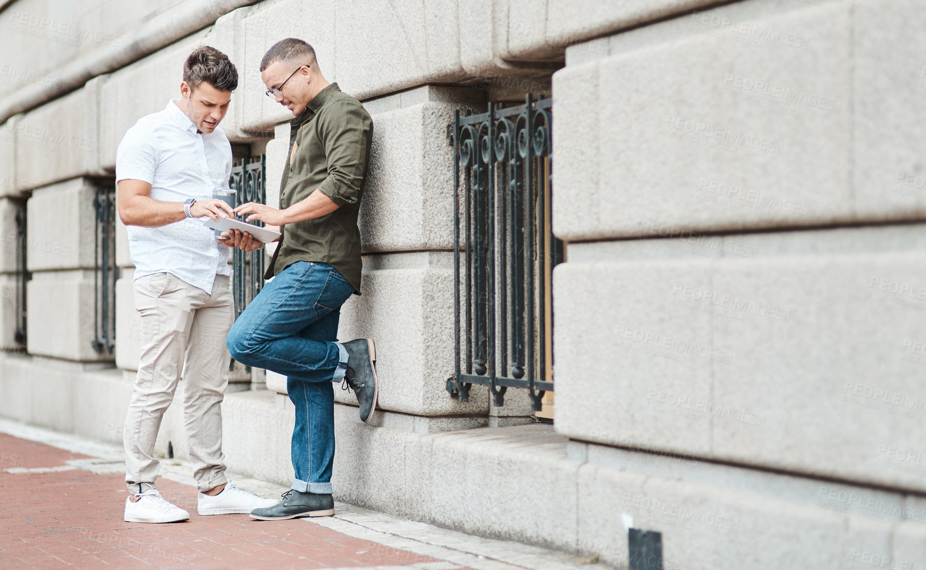 Buy stock photo Shot of two young businessmen using a digital tablet together against an urban background