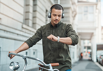 Buy stock photo Shot of a young businessman looking at his watch while riding a bicycle in the city
