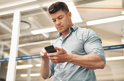 Buy stock photo Cropped shot of a handsome young businessman using his cellphone while standing in the office