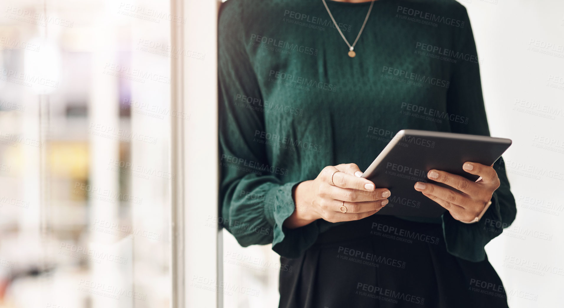 Buy stock photo Cropped portrait of an unrecognizable young businesswoman using her tablet while standing in the office