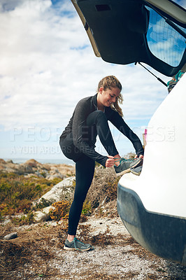 Buy stock photo Shot of a young woman tying her shoelaces on a cars boot outdoors