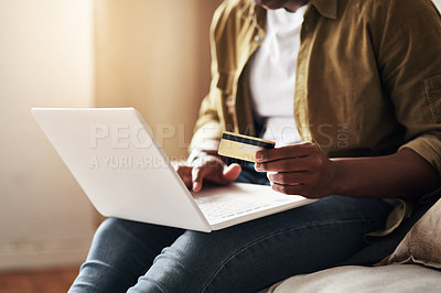Buy stock photo Cropped shot of an unrecognizable man using a laptop and a credit card to shop online while sitting on his couch at home