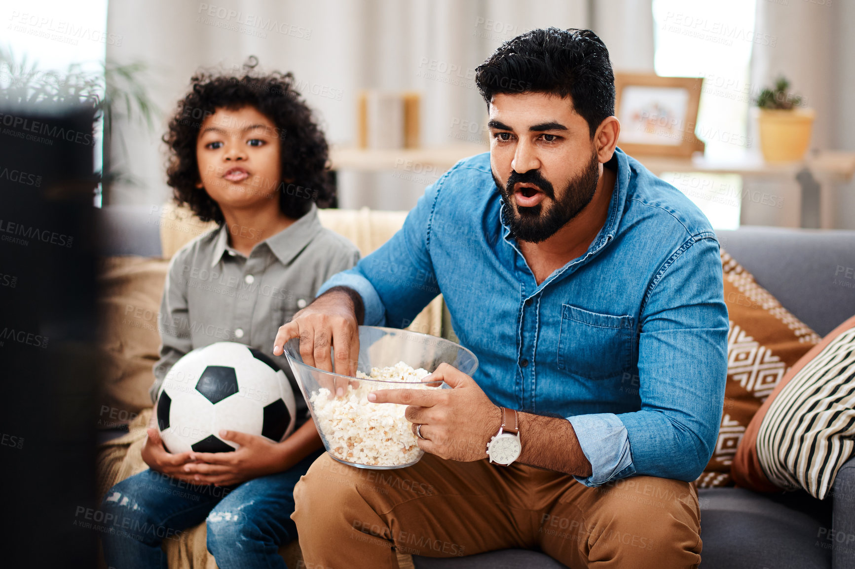 Buy stock photo Cropped shot of an adorable little boy watching a football game with his father on tv at home