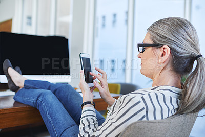Buy stock photo Rearview shot of a mature businesswoman using a cellphone while sitting with her feet up on a desk in an office