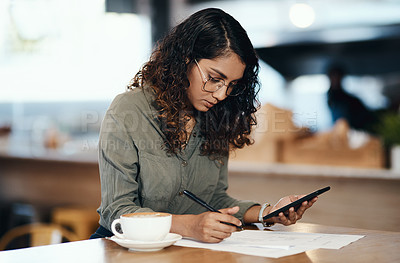 Buy stock photo Small business owner or entrepreneur filling out paper work or a document in an internet cafe or coffee shop with a phone in hand. Young woman writing on a from and sitting at a table in a restaurant