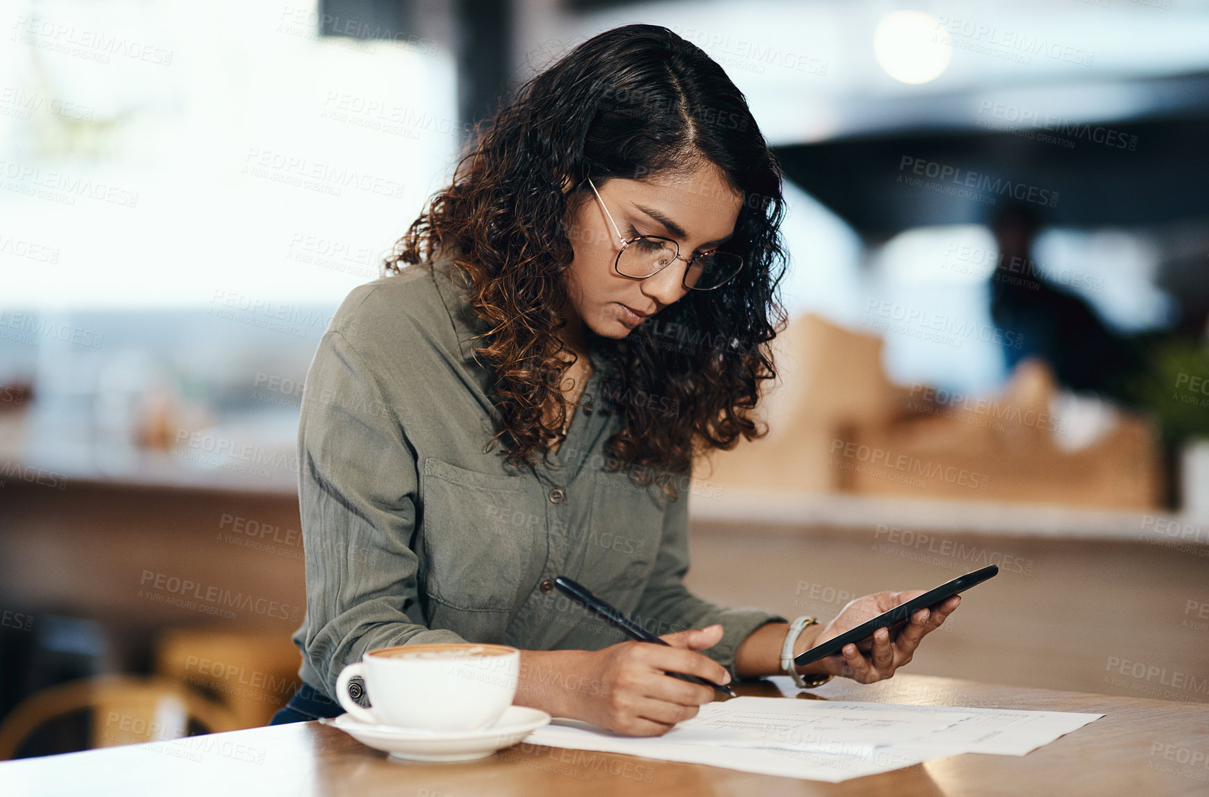 Buy stock photo Small business owner or entrepreneur filling out paper work or a document in an internet cafe or coffee shop with a phone in hand. Young woman writing on a from and sitting at a table in a restaurant
