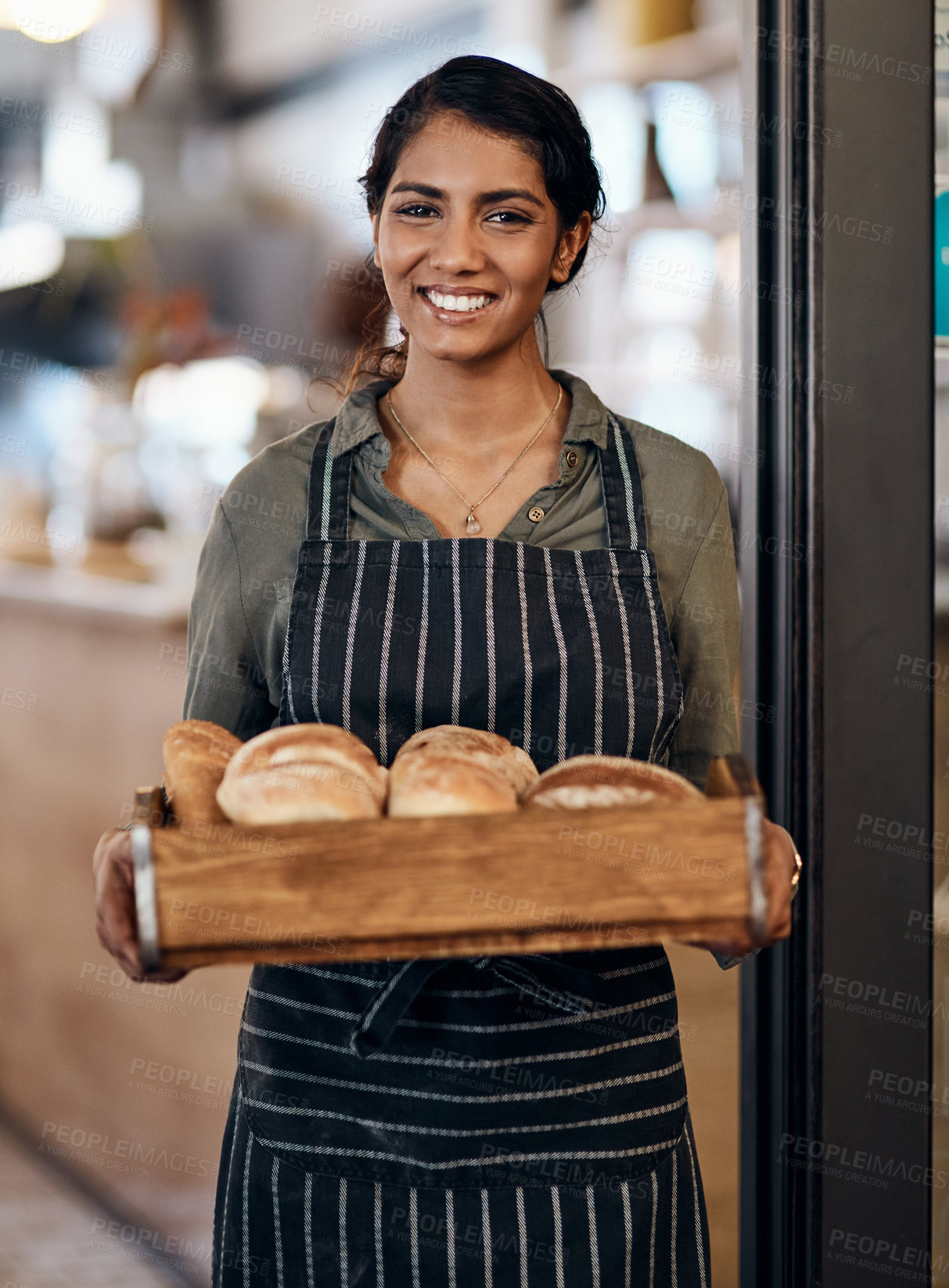 Buy stock photo Shot of a young woman holding a selection of freshly baked breads in her bakery