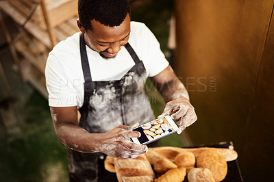 Buy stock photo Cropped shot of a male baker taking a picture on his cellphone of a selection of freshly baked bread