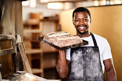 Buy stock photo Cropped shot of a male baker holding up freshly baked bread in his bakery