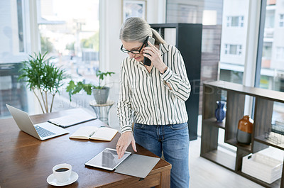 Buy stock photo Shot of a mature businesswoman talking on a cellphone while using a digital tablet in an office