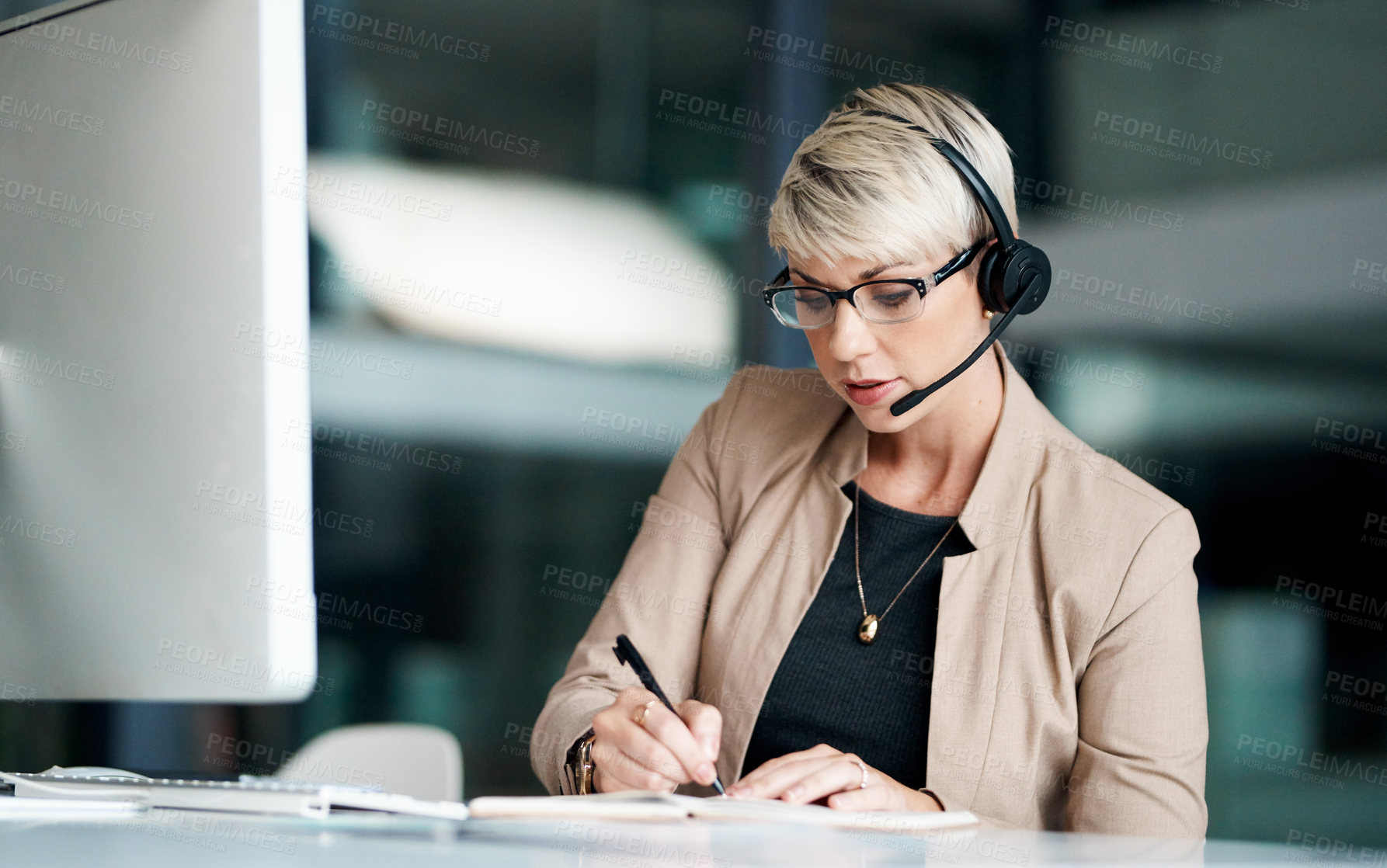 Buy stock photo Shot of a young businesswoman wearing a headset while writing notes in an office