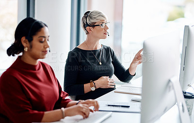 Buy stock photo Shot of a young businesswoman wearing a headset while working on a computer alongside a colleague in an office