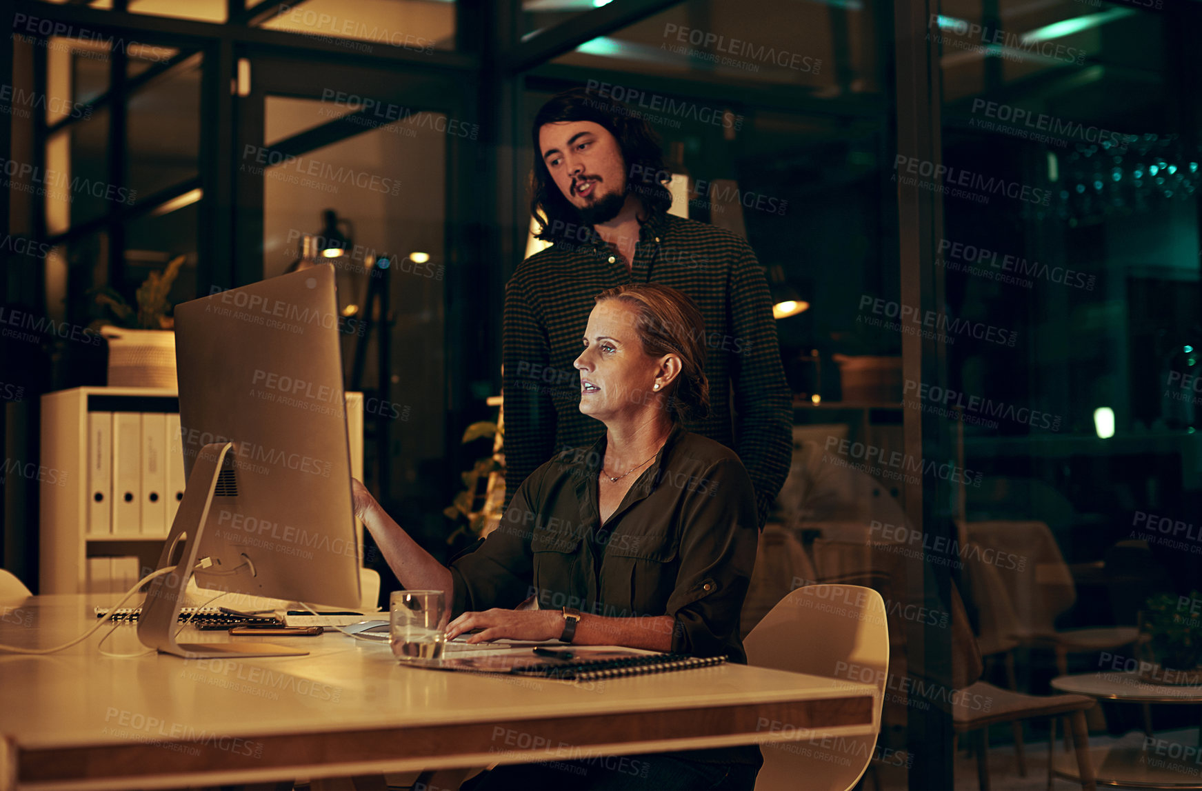 Buy stock photo Shot of two businesspeople looking at something on a computer in an office at night
