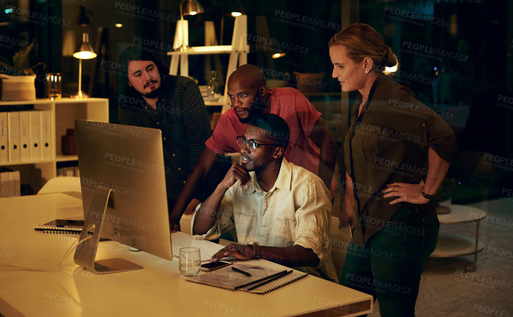 Buy stock photo Shot of a group of businesspeople looking at something on a computer in an office at night