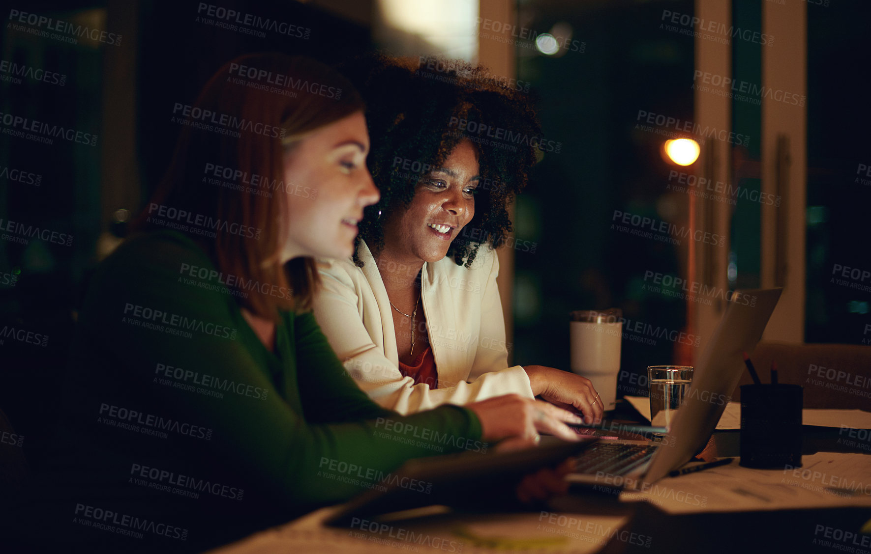 Buy stock photo Shot of two businesswomen working together in an office at night