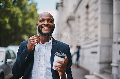Buy stock photo Shot of a businessman holding a coffee and listening to music through earphones while walking through the city
