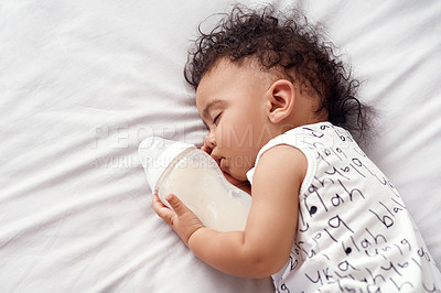 Buy stock photo Shot of an adorable baby boy sleeping with his bottle of milk on the bed at home