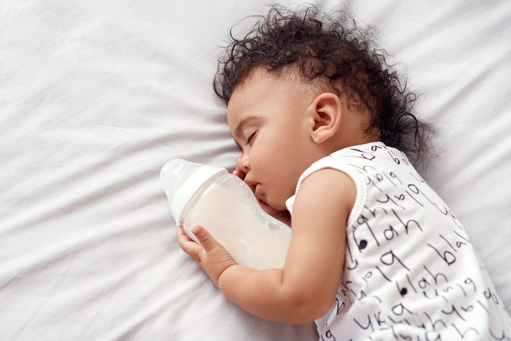 Buy stock photo Shot of an adorable baby boy sleeping with his bottle of milk on the bed at home