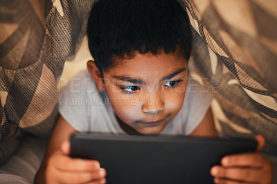 Buy stock photo Shot of an adorable little boy using a digital tablet while lying under a blanket at home