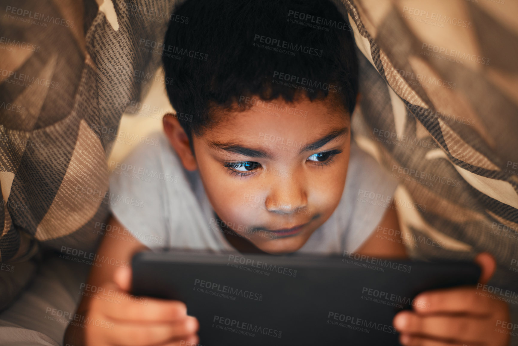 Buy stock photo Shot of an adorable little boy using a digital tablet while lying under a blanket at home