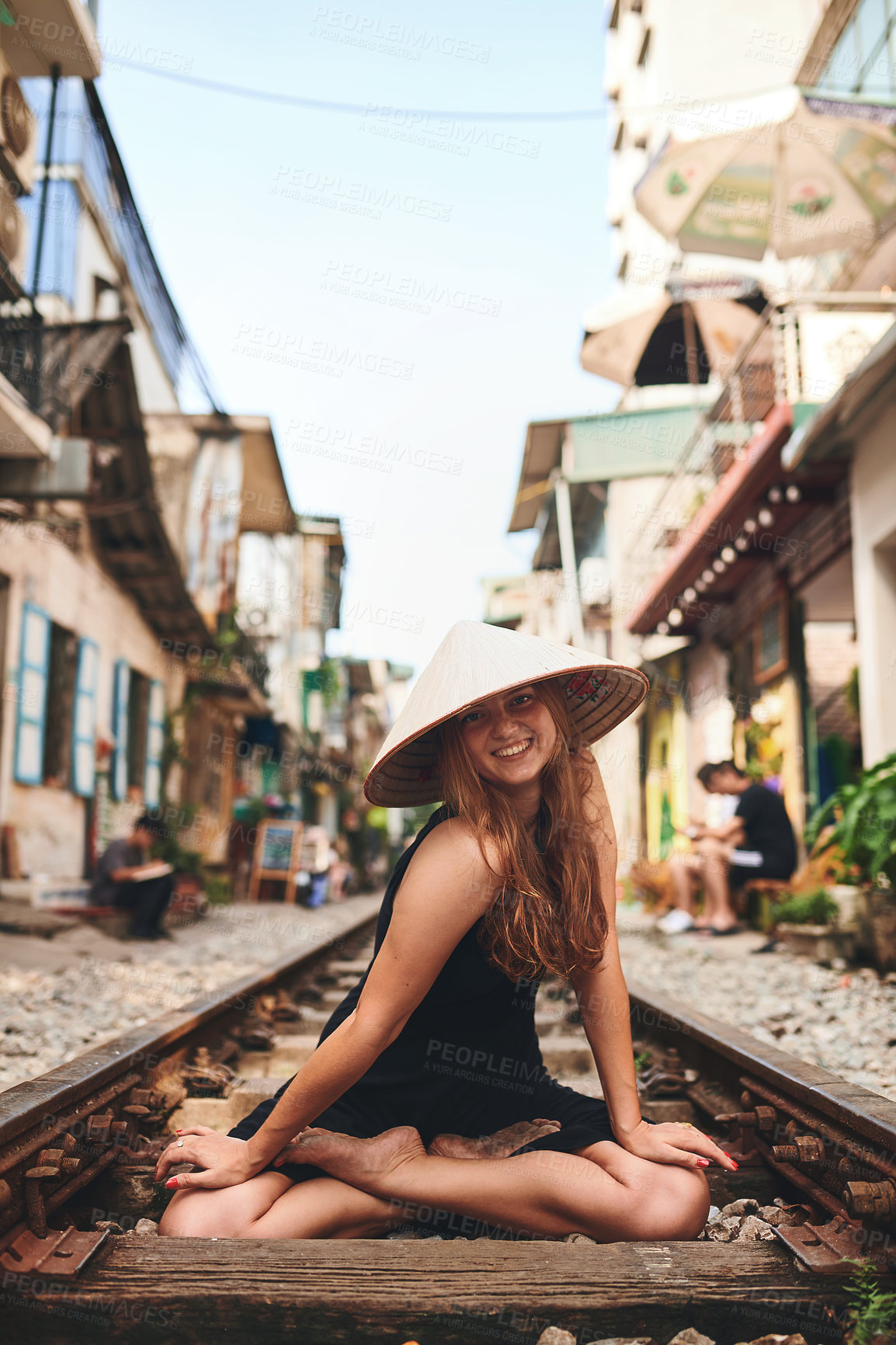 Buy stock photo Shot of a woman wearing a conical hat while sitting on a railway track