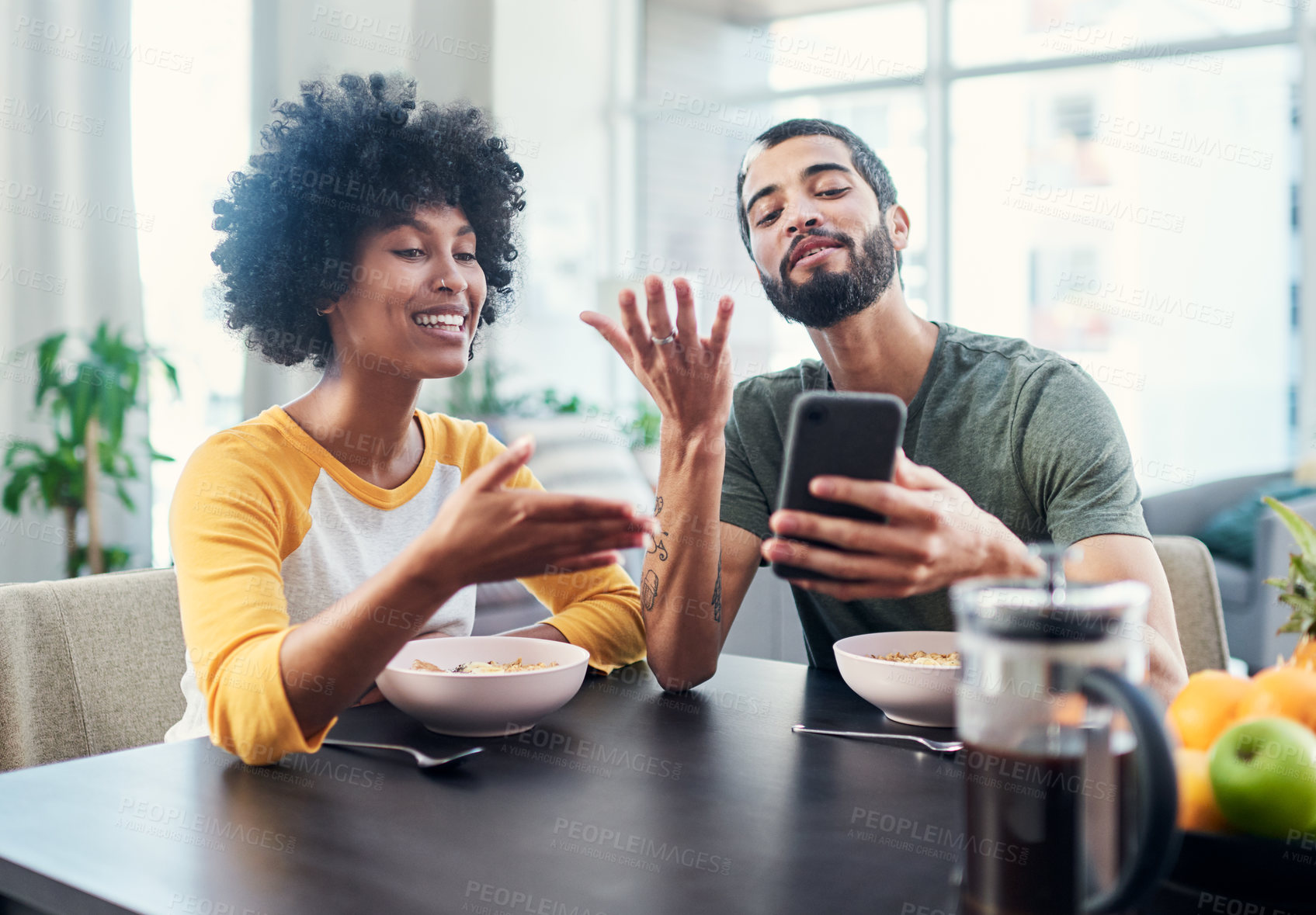 Buy stock photo Shot of a young couple looking at something on a cellphone while having breakfast at home