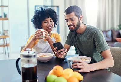 Buy stock photo Shot of a young couple looking at something on a cellphone while having breakfast at home