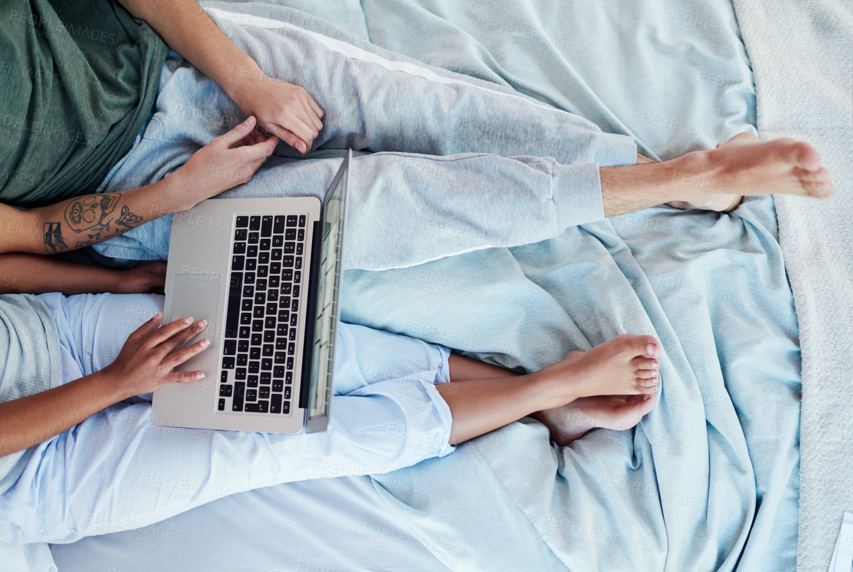 Buy stock photo Cropped shot of an unrecognizable couple using a laptop while sitting on their bed