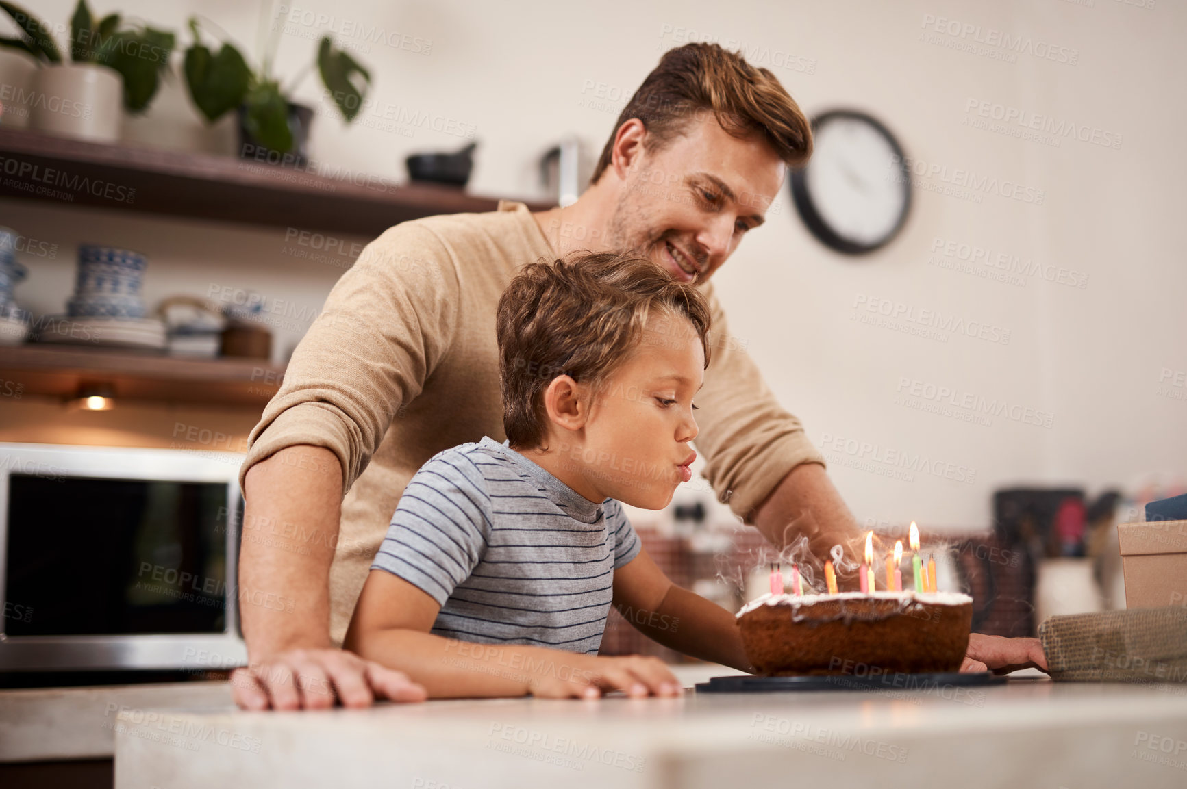 Buy stock photo Shot of a boy blowing out the candles on his birthday cake while celebrating with his dad