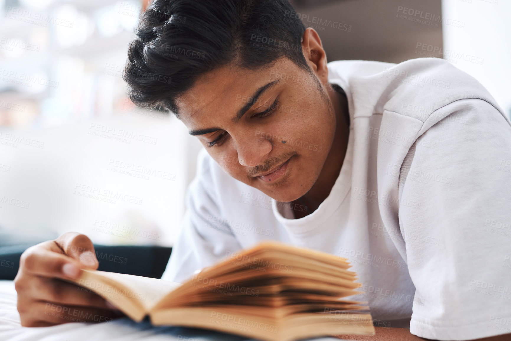 Buy stock photo Cropped shot of a young man reading a book while lying on his bed
